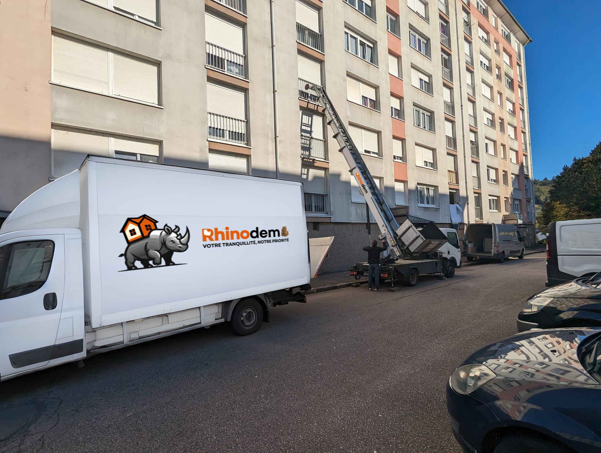 Au premier plan, un camion de déménagement Rhinodem, flanqué d'un monte-meubles.