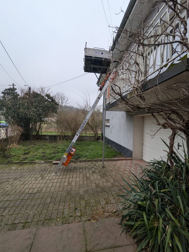 Location de monte-meubles à Nancy : monte-meubles en cours d’utilisation devant une maison à étage. L’équipement, positionné sur l’allée pavée, permet de faire monter ou descendre des objets volumineux depuis un balcon situé au premier étage.