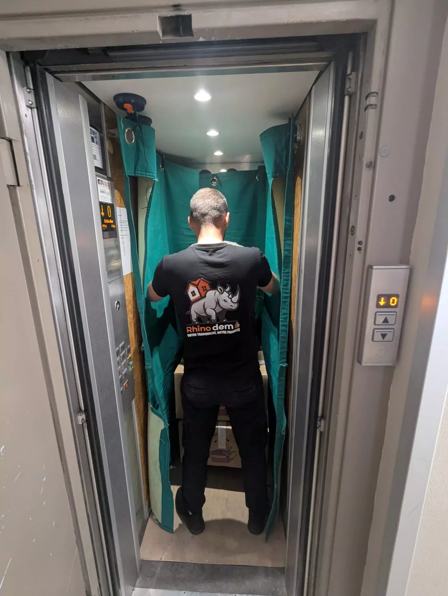 Un déménageur protège un ascenseur avec des housses